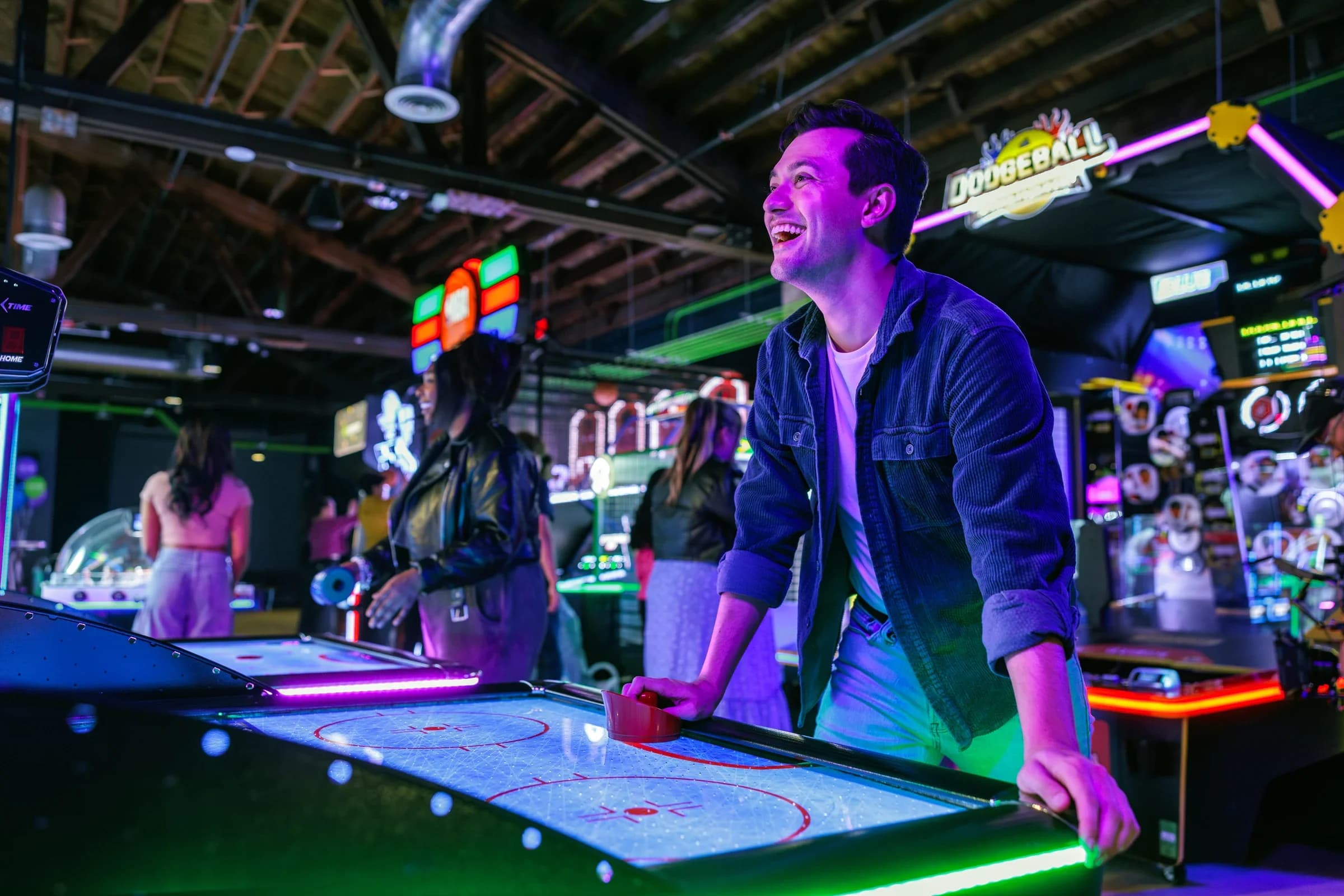 A guest laughing at an air hockey table under neon lighting at Ignite Arcade.