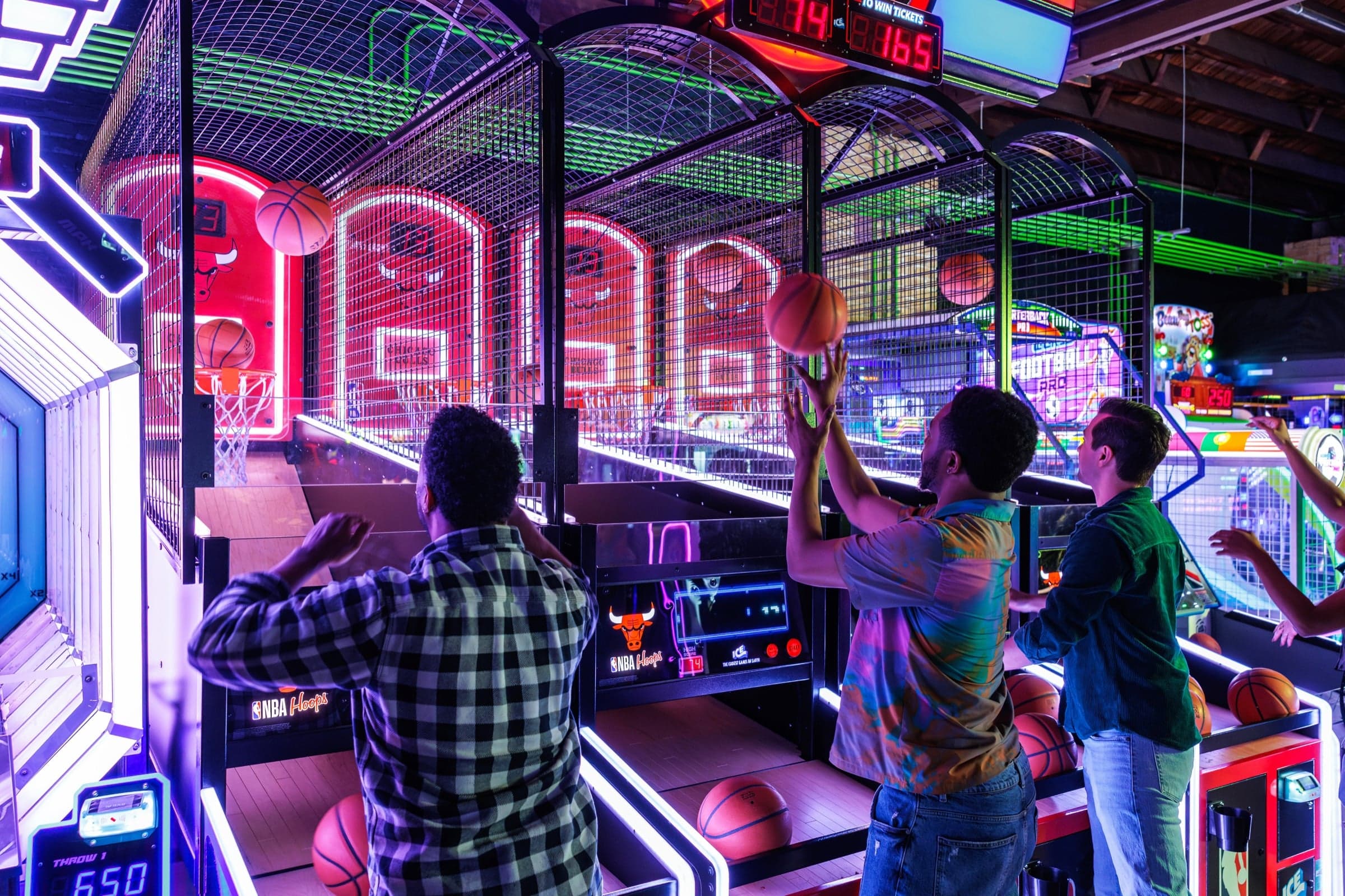 Three players at the basketball arcade game on Ignite Arcade's neon-lit games floor.