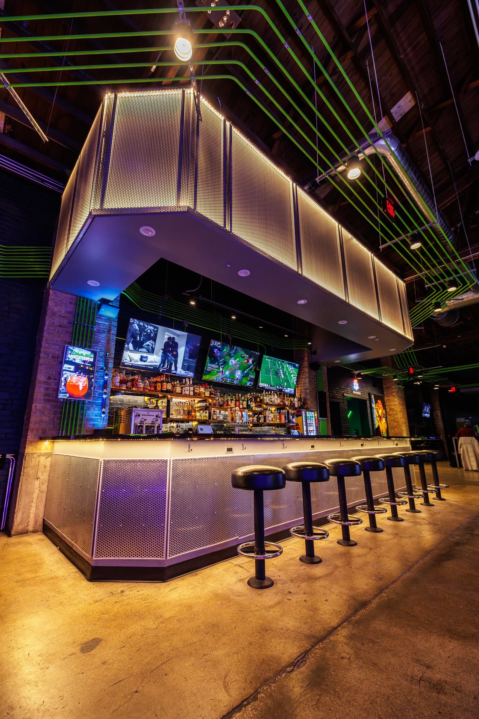 Bar at Ignite Arcade with stools under green neon lighting.