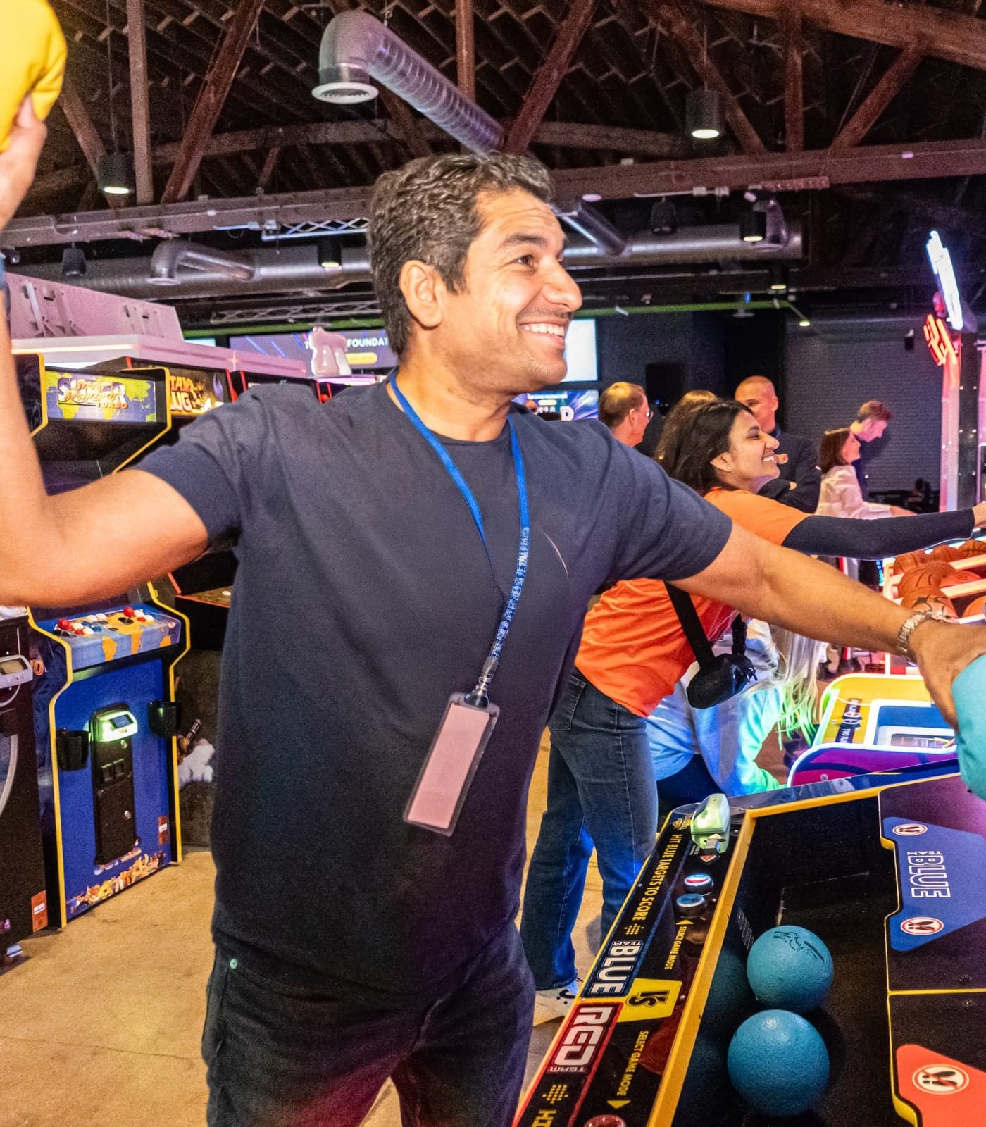 A corporate-event guest tossing a ball at an arcade game while his group plays behind him.