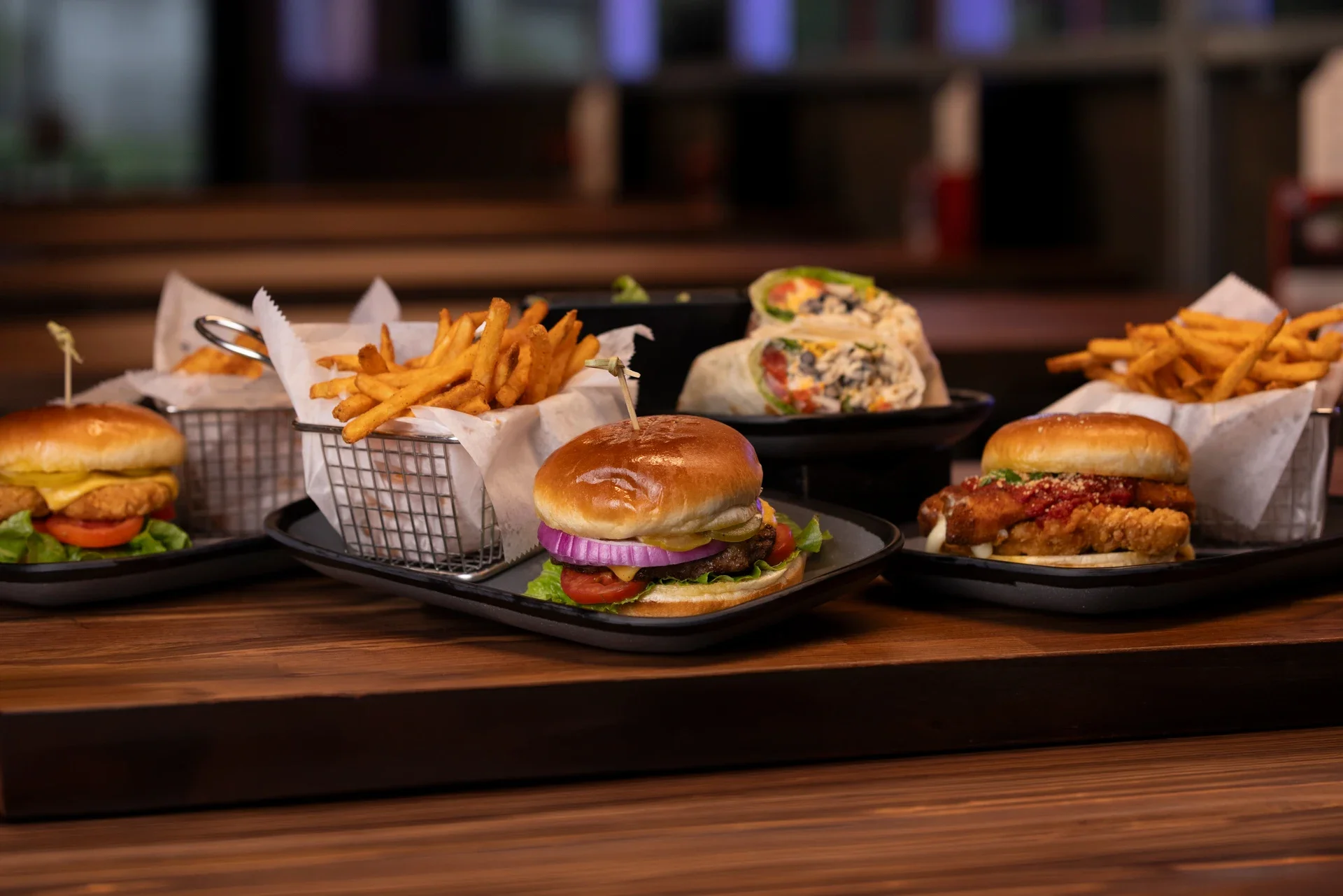 Cheeseburger sliders, seasoned fries, a chicken parmesan slider, and a veggie wrap on trays at Ignite Arcade.