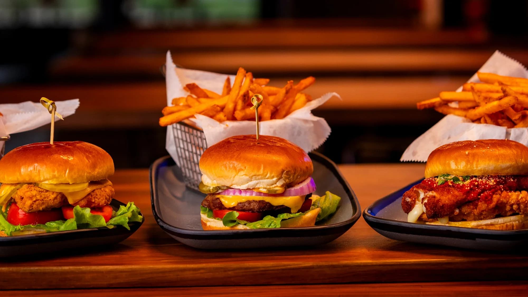Three sliders with side baskets of fries at Ignite Arcade: crispy chicken, cheeseburger, and spicy chicken.