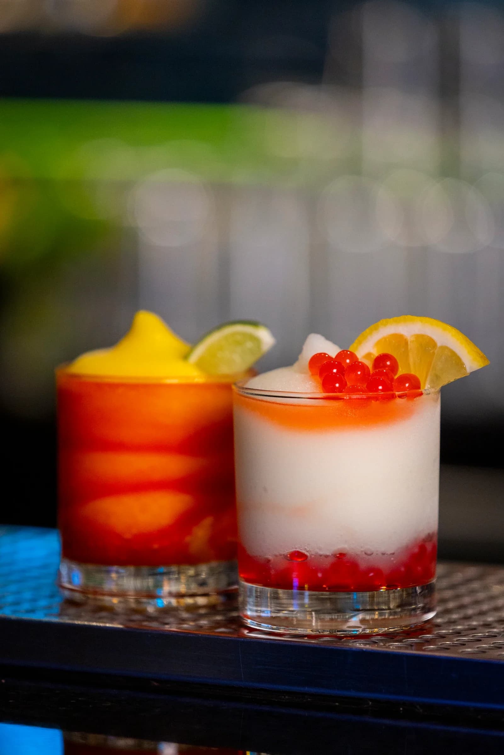 Two Ignite Arcade signature cocktails: an orange sunset tumbler and a frosty white drink with red boba pearls and lemon.