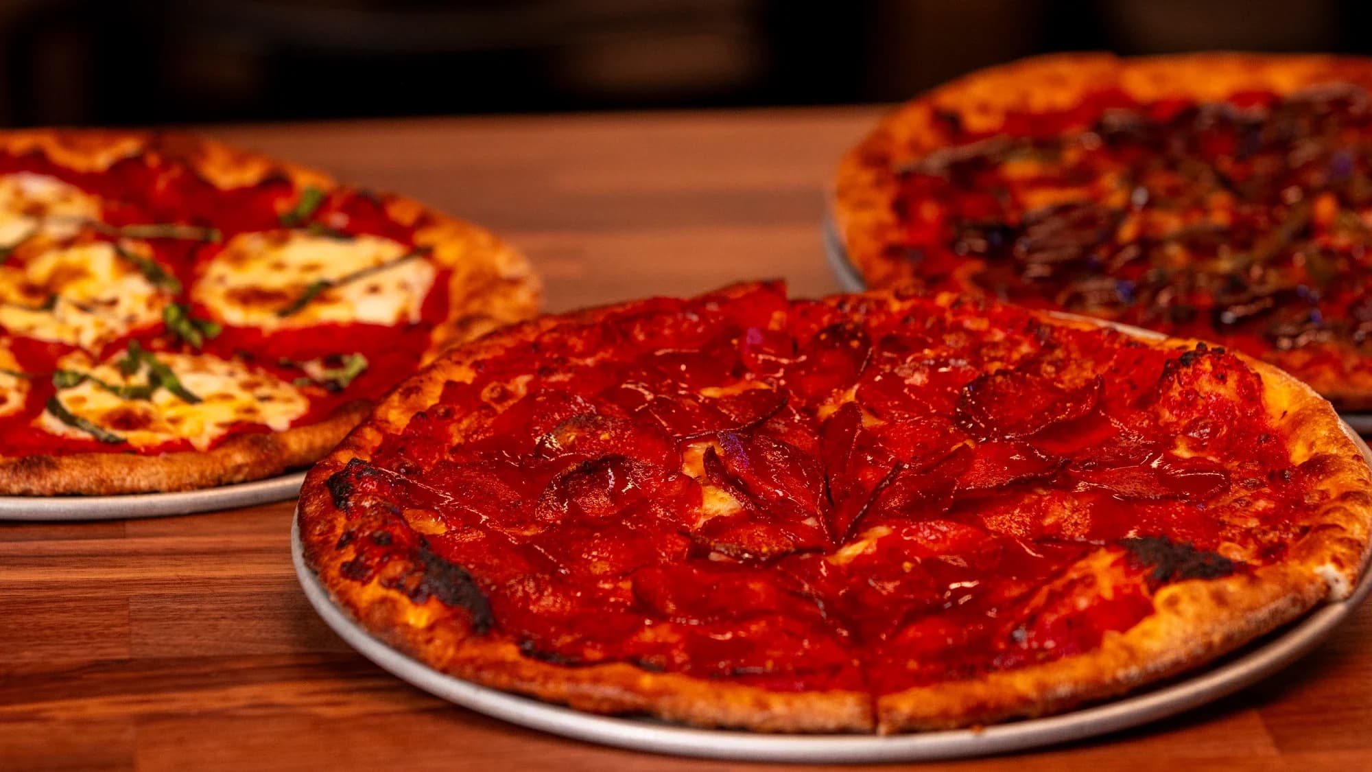Margherita, pepperoni, and barbecue pizzas on a wood table at Ignite Arcade.