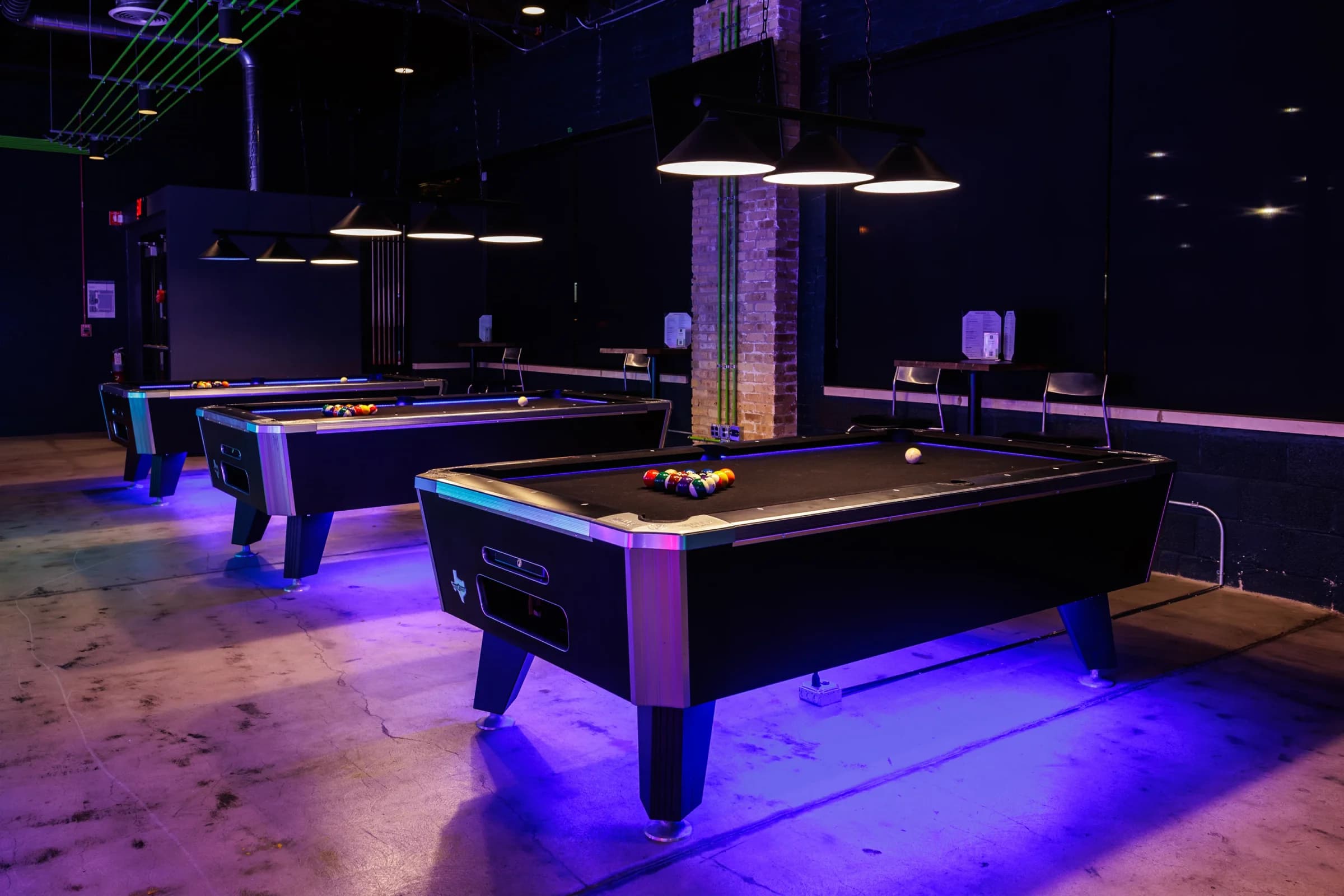 Three black-top pool tables with neon under-lighting at Ignite Arcade.